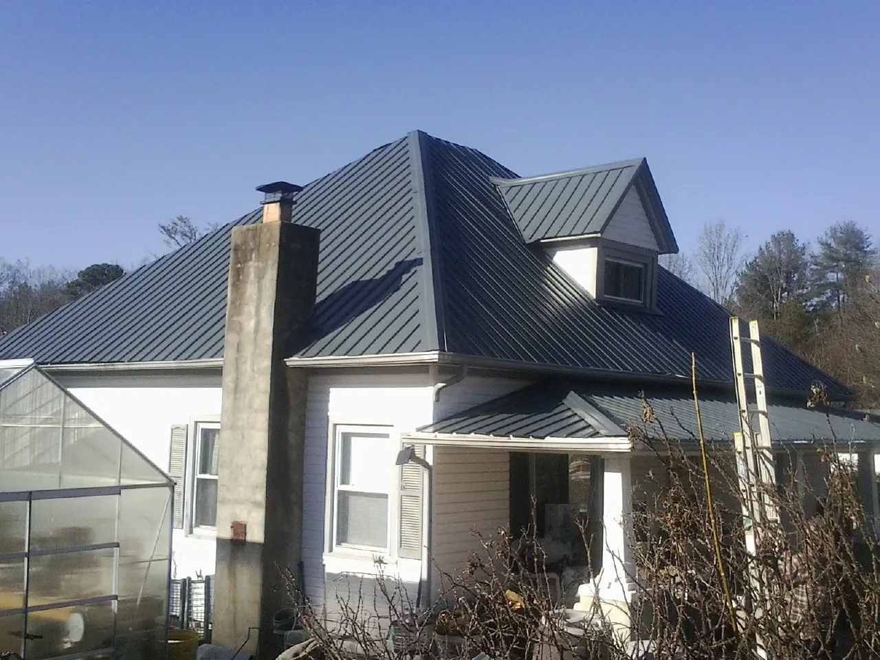 Dark blue standing seam metal roof on a white farmhouse with dormer — Slate & Tile Roof Repair by Roofing Brothers in Tall Timbers