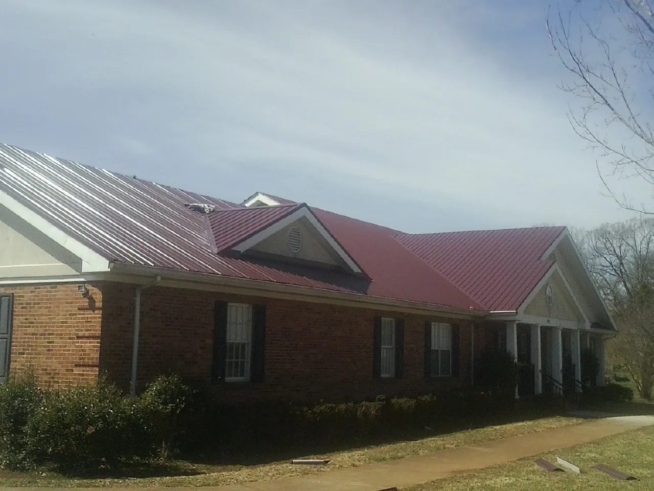 Red metal roof with gabled entries on a long brick building, from a Hail Damage Roof Repair job in Tall Timbers