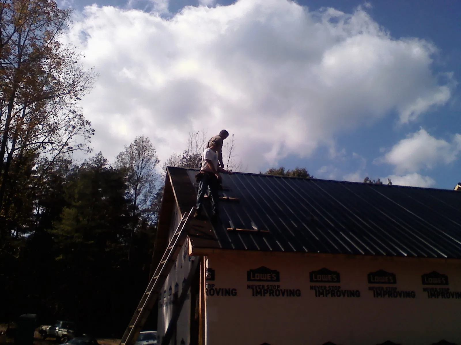 Roofer fastening dark metal panels high against a cloudy sky, from a Roof Inspection job in Tall Timbers