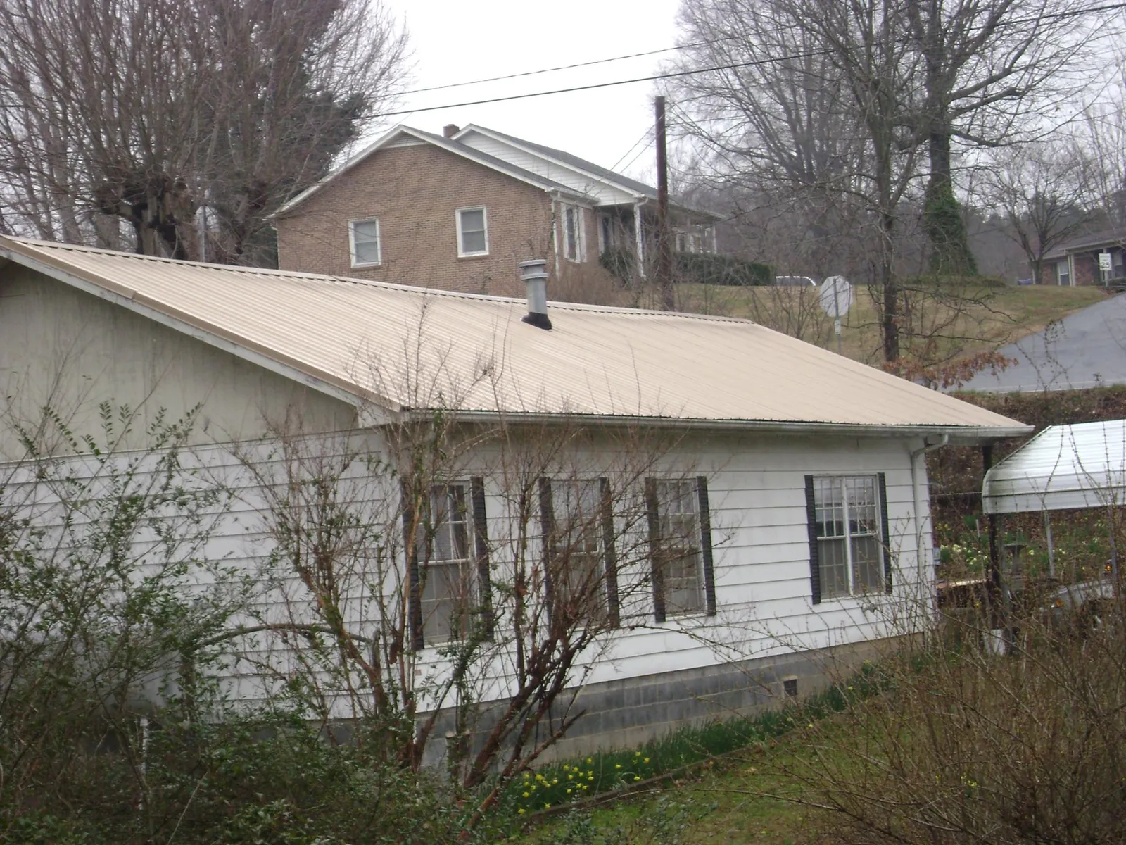 Tan metal roof on a white sided house set into a hillside — Commercial Roofing by Roofing Brothers in Tall Timbers