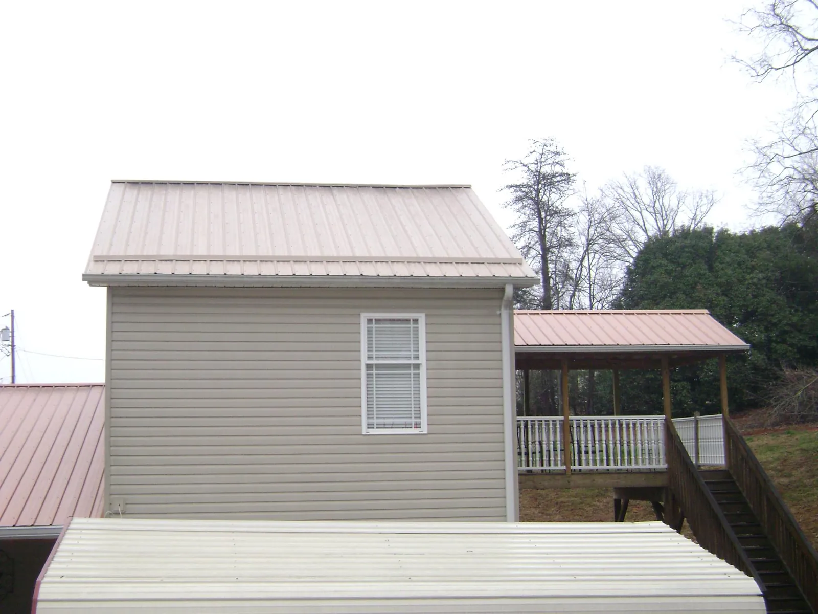 Tan metal roofs on a two story addition and attached porch, from a Roof Replacement job in Tall Timbers